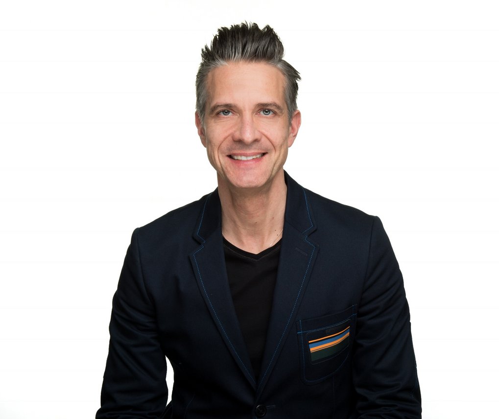 Man in dark blazer against white background.