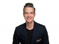 Man in dark blazer against white background.