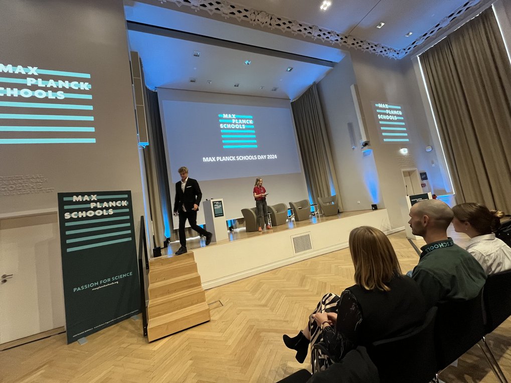Bühne bei Max Planck Schools Day 2024 mit Präsentation und Publikum im Konferenzsaal.