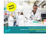 A lab setup with several people in the background and one person with a pipette in the front.