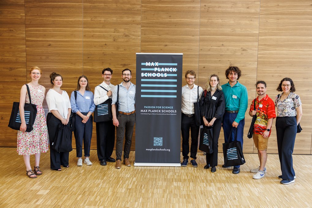 Absolventen stehen vor einem Poster der Max Planck Schools