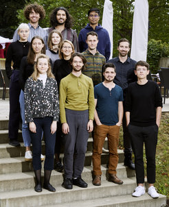 Eine Gruppe von Personen steht auf einer Treppe im Freien, mit verschiedenen Outfits, umgeben von Bäumen.