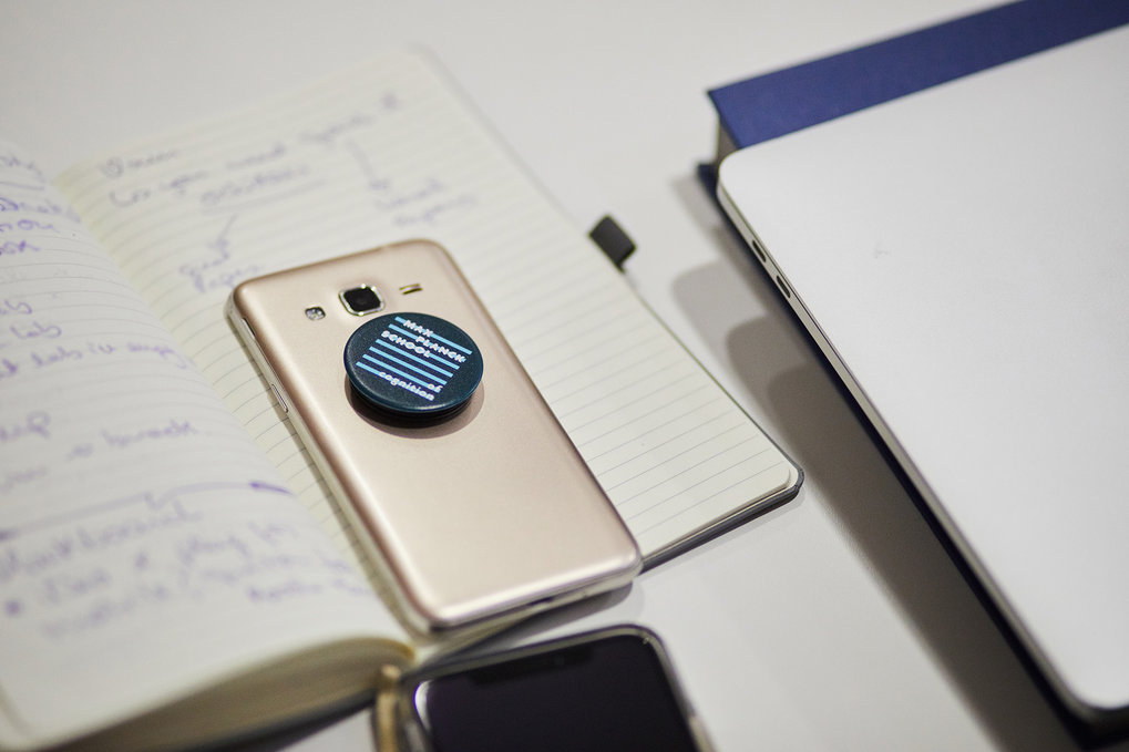 Smartphone mit PopSocket auf offenem Notizbuch, Laptop daneben.