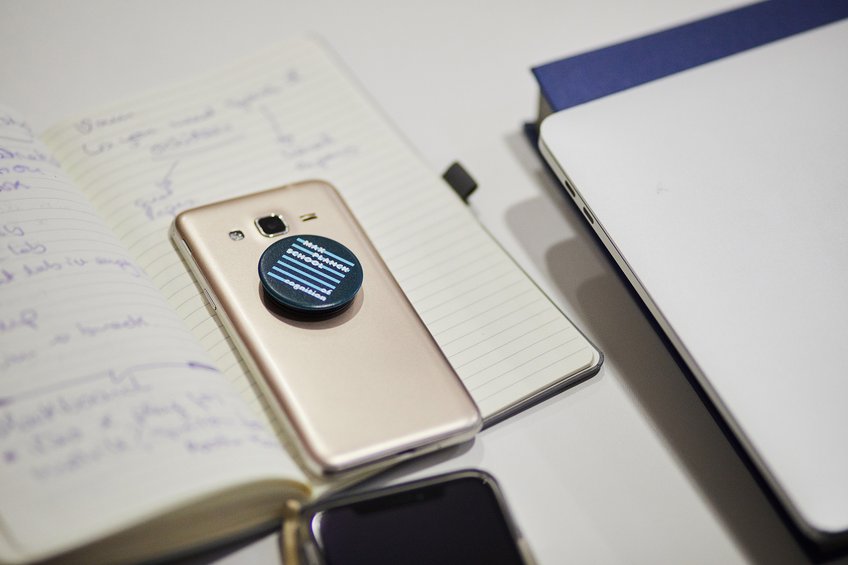Fast-Track-Programm für Bachelor-Kandidaten Smartphone mit PopSocket auf offenem Notizbuch, Laptop daneben.